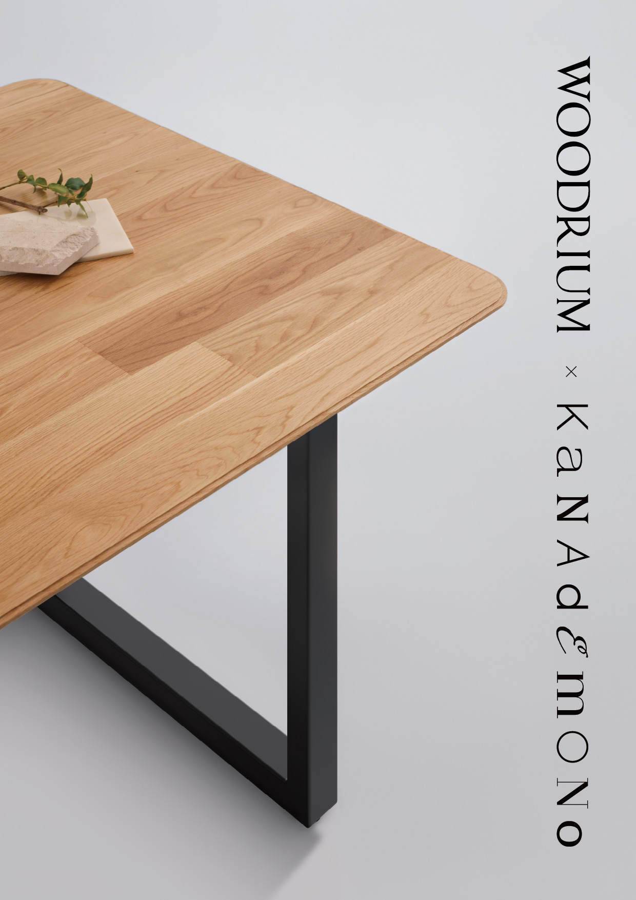 Angled view of a light oak desk with a black metal leg against a pale gray background; vertical branding along the right edge.